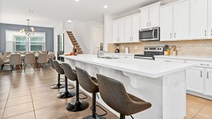 Une cuisine moderne avec des meubles blancs, un grand îlot central doté de tabourets, un four à micro-ondes et un évier.