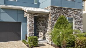 Une maison moderne avec une façade en pierre, un garage et un jardin bien entretenu, agrémenté d’arbustes et d’un palmier.