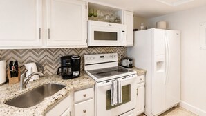 A compact kitchen with white cabinetry, a microwave, a stove, a coffee maker, and a refrigerator. - Park Shore Resort-2nd Floor BLDG J #255*Lake view* (Park Shore Resort)