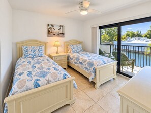 A room with two beds, a nightstand, a lamp, and a view of a body of water through large windows. - Park Shore Resort-2nd Floor BLDG J #255*Lake view* (Park Shore Resort)