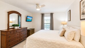 A bedroom with a bed, dresser, TV, ceiling fan, and window with curtains. - Park Shore Resort-2nd Floor BLDG J #255*Lake view* (Park Shore Resort)