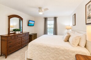 Ein Schlafzimmer mit Bett, Schminktisch, Fernseher, Deckenventilator und Fenster mit Vorhängen.