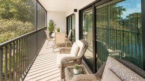 A balcony with wicker furniture, a table with a plant, and a view of trees and buildings. - Park Shore Resort-2nd Floor BLDG J #255*Lake view* (Park Shore Resort)