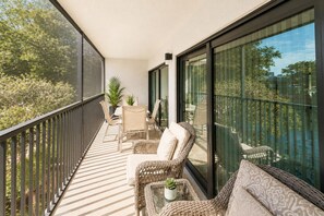 Ein Balkon mit Korbmöbeln, einem Tisch mit einer Pflanze und Blick auf Bäume und Gebäude.