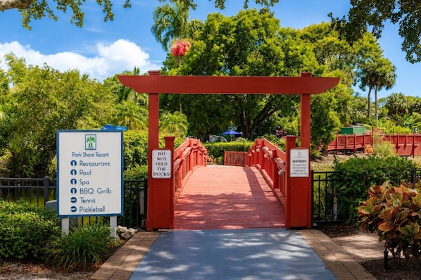 A red archway leading to a park with a sign listing amenities like a restaurant, pool, spa, BBQ grills, tennis, and pickleball.
