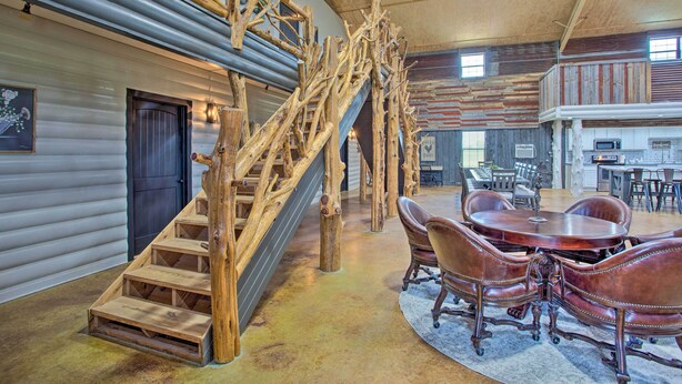Un interior rústico con una escalera de madera, un comedor con sillas de cuero y una cocina al fondo.