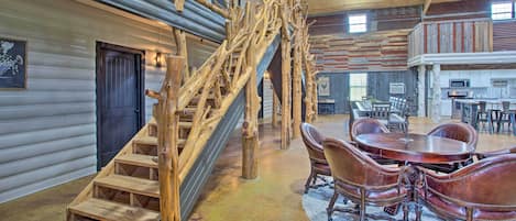 A rustic interior with a wooden staircase, a dining area with leather chairs, and a kitchen in the background.