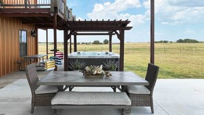 Un patio con una pérgola de madera, un jacuzzi, mobiliario de mimbre y vistas al campo.