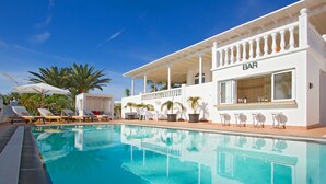 Un área junto a la piscina con sillones de descanso, un bar y una zona de estar cubierta.
