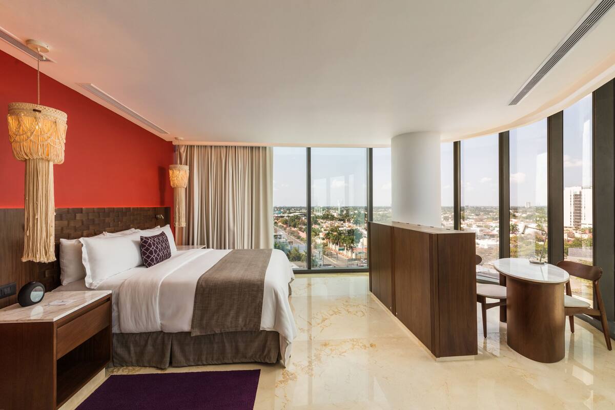 A modern hotel room with a large bed, a desk, and a view of the city.