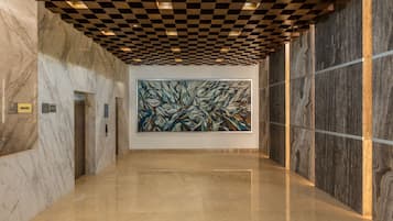 A hallway with marble walls, a large abstract painting, and a checkered ceiling.
