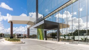 A modern building with a glass facade, a covered entrance, and a landscaped area with plants. - Camino Real Mérida (Mérida)