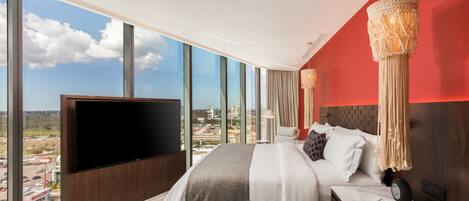 Una habitación de hotel moderna con una cama grande, un televisor de pantalla plana y vistas a la ciudad a través de grandes ventanales.
