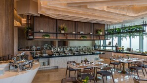 A modern restaurant with a buffet area, wooden paneling, and a variety of plants. - Camino Real Mérida (Mérida)