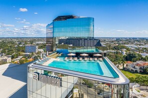 Un hôtel moderne doté d’une piscine sur le toit, offrant une vue dégagée sur la ville et se distinguant par sa façade en verre imposante.