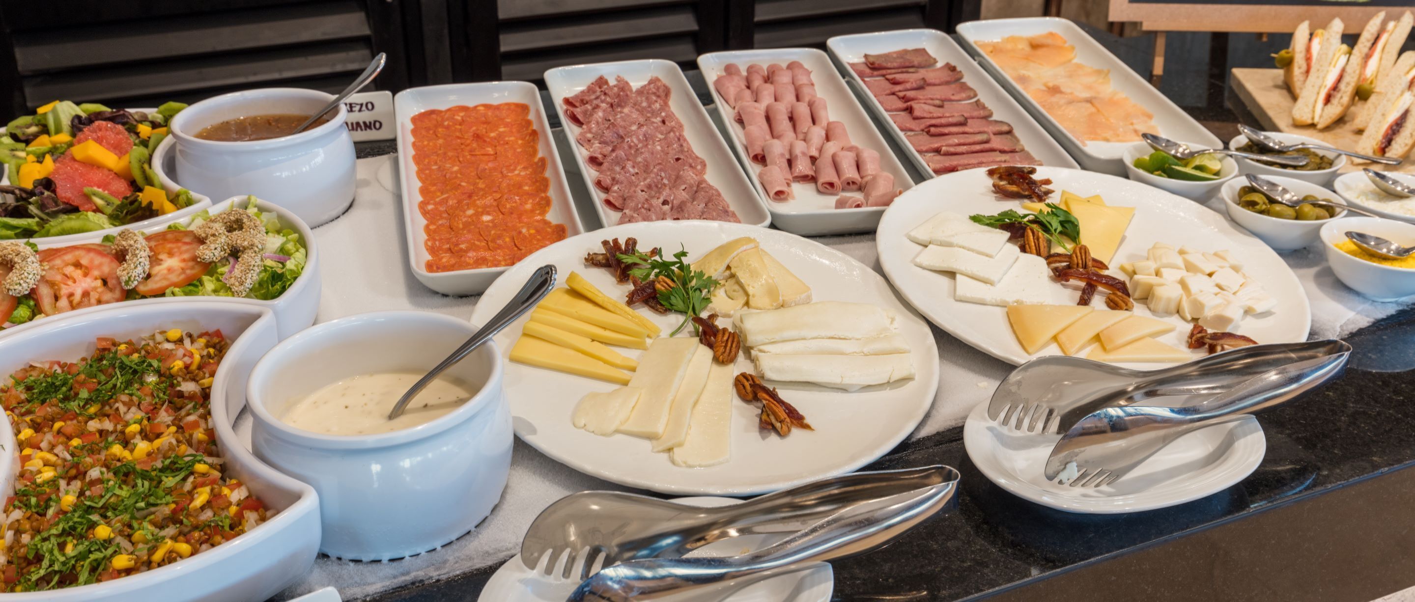 A buffet with various food items including salads, meats, cheeses, and dips.