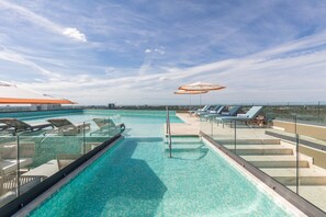 A rooftop infinity pool with lounge chairs and umbrellas, offering a view of the city skyline.