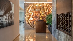 A modern hotel lobby with a reception desk, a large abstract mural, and a staircase leading to upper floors. - Camino Real Mérida (Mérida)