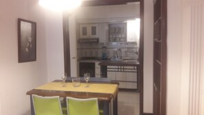 Un área de comedor con una mesa preparada para dos personas, dos sillas y dos copas de vino.