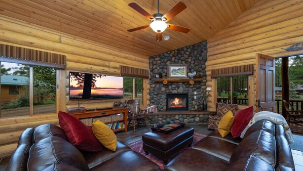 A cozy log cabin interior with a stone fireplace, leather sofas, and a television. - 2 Blue Feather in Beautiful Greer AZ (Greer)