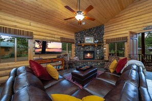 A cozy log cabin interior with a stone fireplace, leather sofas, and a television. - 2 Blue Feather in Beautiful Greer AZ (Greer)