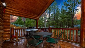 A covered wooden deck with a grill, green metal chairs, and a view of a forested area. - 2 Blue Feather in Beautiful Greer AZ (Greer)