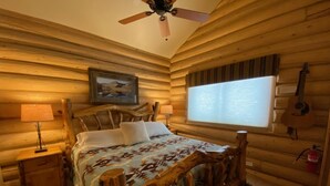A log cabin bedroom with a bed, wooden headboard, a ceiling fan, a window, and a guitar on the wall. - 2 Blue Feather in Beautiful Greer AZ (Greer)