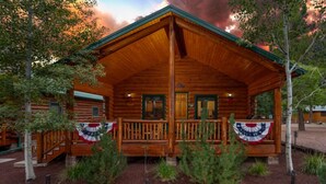 A wooden cabin with a porch, surrounded by trees and a flag. - 2 Blue Feather in Beautiful Greer AZ (Greer)