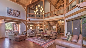 A spacious living area with a high ceiling, wooden beams, a chandelier, and a large window. - Grand Angel Fire Retreat w/ Hot Tub & Fire Pit! (Angel Fire)