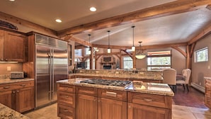 A spacious kitchen with granite countertops, wooden cabinets, a stainless steel refrigerator, and a large island with a gas stove. - Grand Angel Fire Retreat w/ Hot Tub & Fire Pit! (Angel Fire)