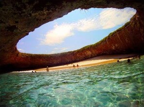 Una playa con agua cristalina y la entrada de una cueva.