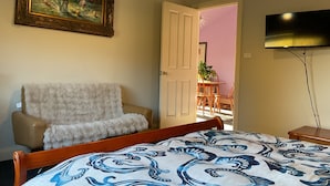 Une chambre à coucher comprenant un lit, une chaise, un tableau, un téléviseur et une porte ouverte donnant sur un balcon.