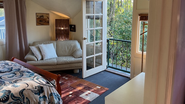 Une chambre avec un canapé, un lit, un tapis à motifs et une porte donnant sur un balcon avec vue sur les arbres.