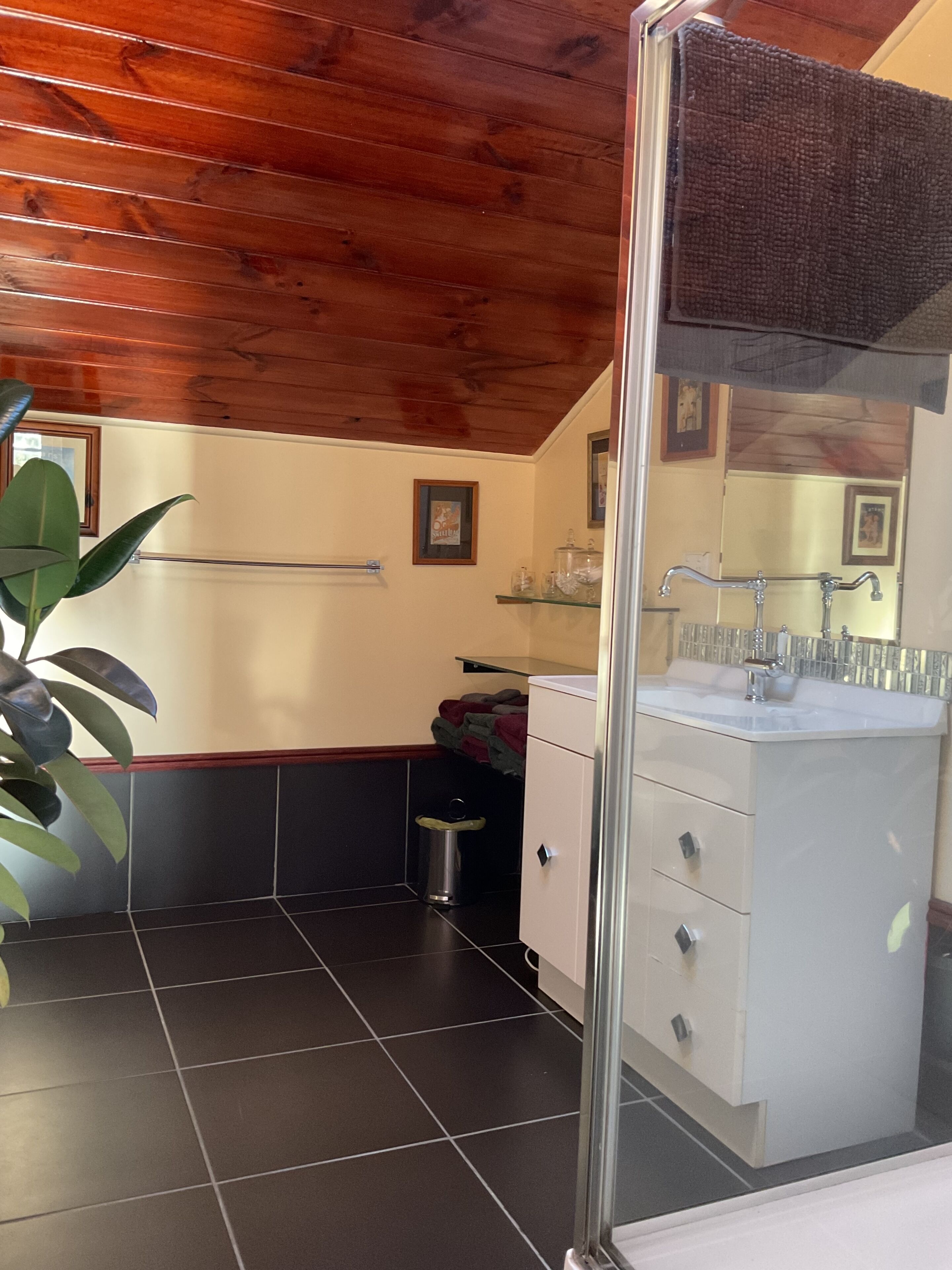 A bathroom with a wooden ceiling, a white sink, a mirror, and a trash bin.