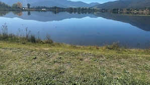 Un lac paisible, avec des montagnes en arrière-plan, un ciel dégagé et un premier plan verdoyant.