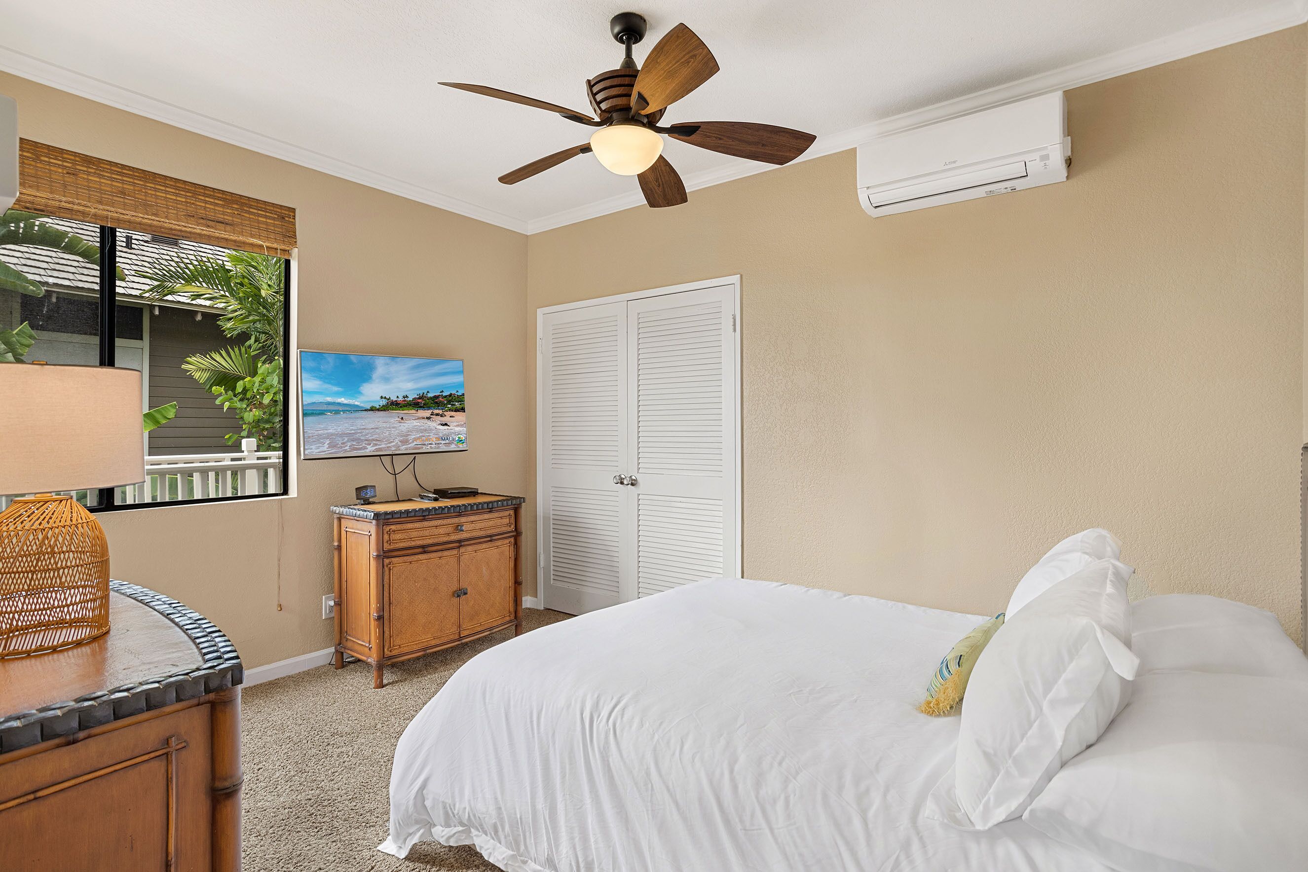 A bedroom with a bed, a ceiling fan, a dresser, a TV, and a window with a view of a beach.