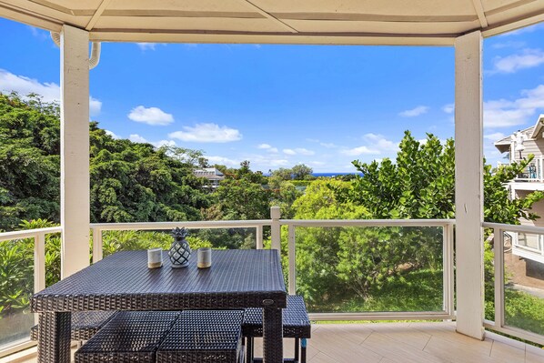 A covered outdoor area with a table and chairs, a railing, and a view of greenery and buildings.