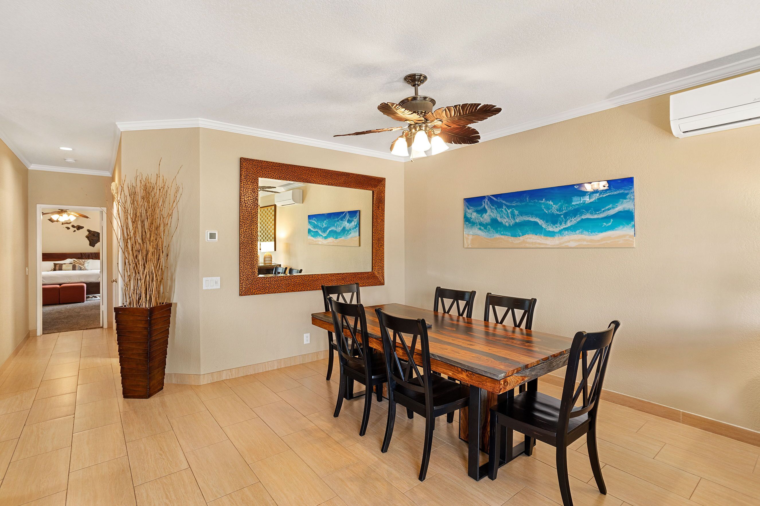 Un coin repas avec une table et des chaises en bois, un ventilateur de plafond et un grand miroir au mur.