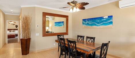 Un coin repas avec une table et des chaises en bois, un ventilateur de plafond et un grand miroir au mur.