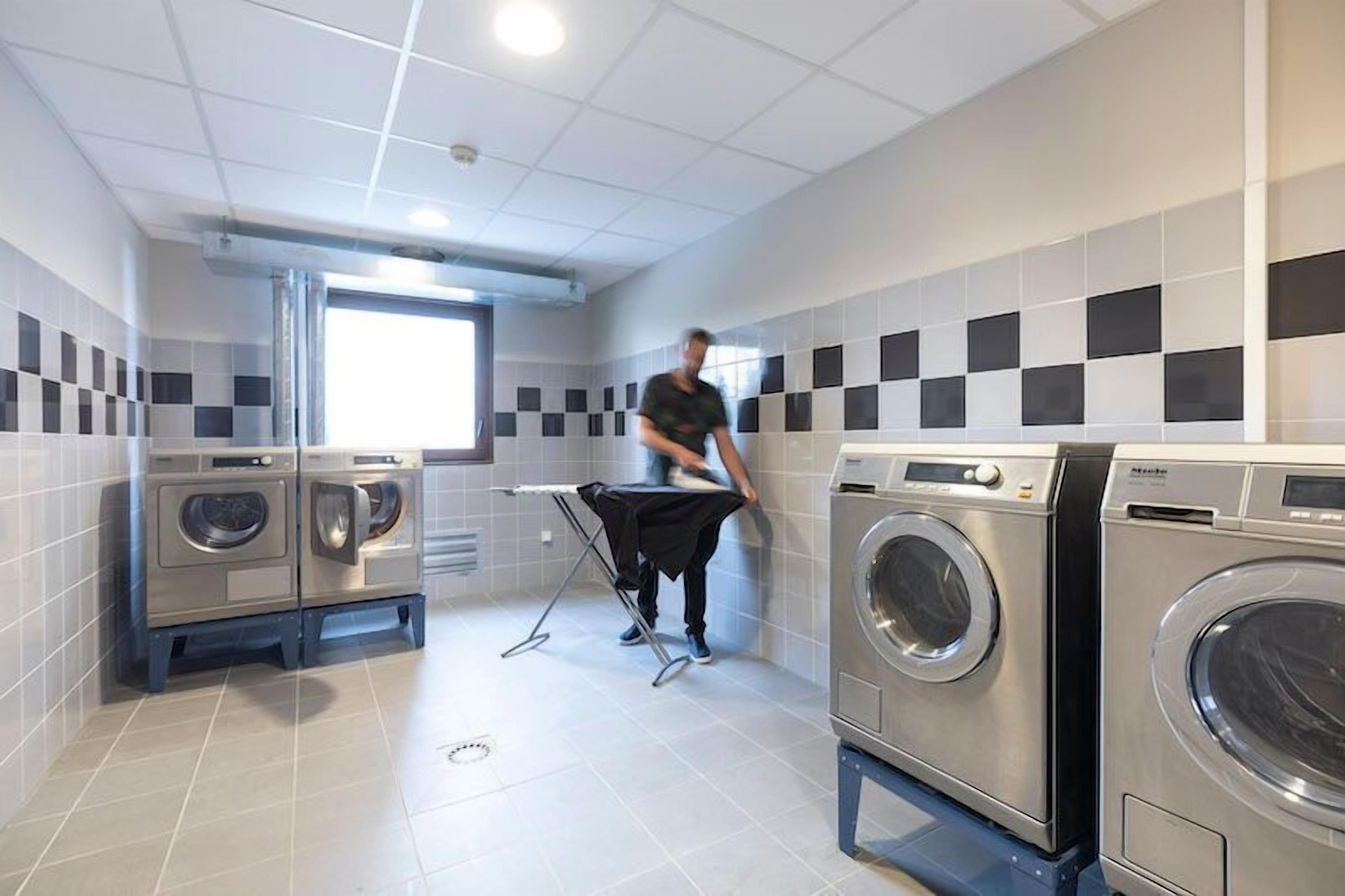 A laundry room with multiple washing machines, a drying rack, and a window providing natural light.