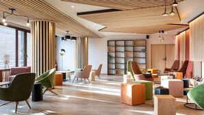 A modern lounge area with wooden slatted ceilings, colorful seating, and a large window providing natural light. - Appartement Confortable Au Pied des Pistes | Wi-Fi Gratuit + Parking Disponible (Villarembert)