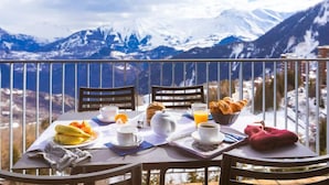 A breakfast setup on a balcony with a mountain view. - Appartement Confortable Au Pied des Pistes | Wi-Fi Gratuit + Parking Disponible (Villarembert)