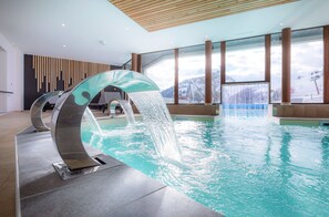 En inomhuspool med en modern vatteninstallation och stora fönster som ger utsikt över snöklädda berg.