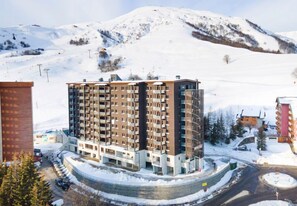 Et moderne, flere etagers hotel beliggende i et snækkedækket bjergområde med en skibakke i baggrunden.
