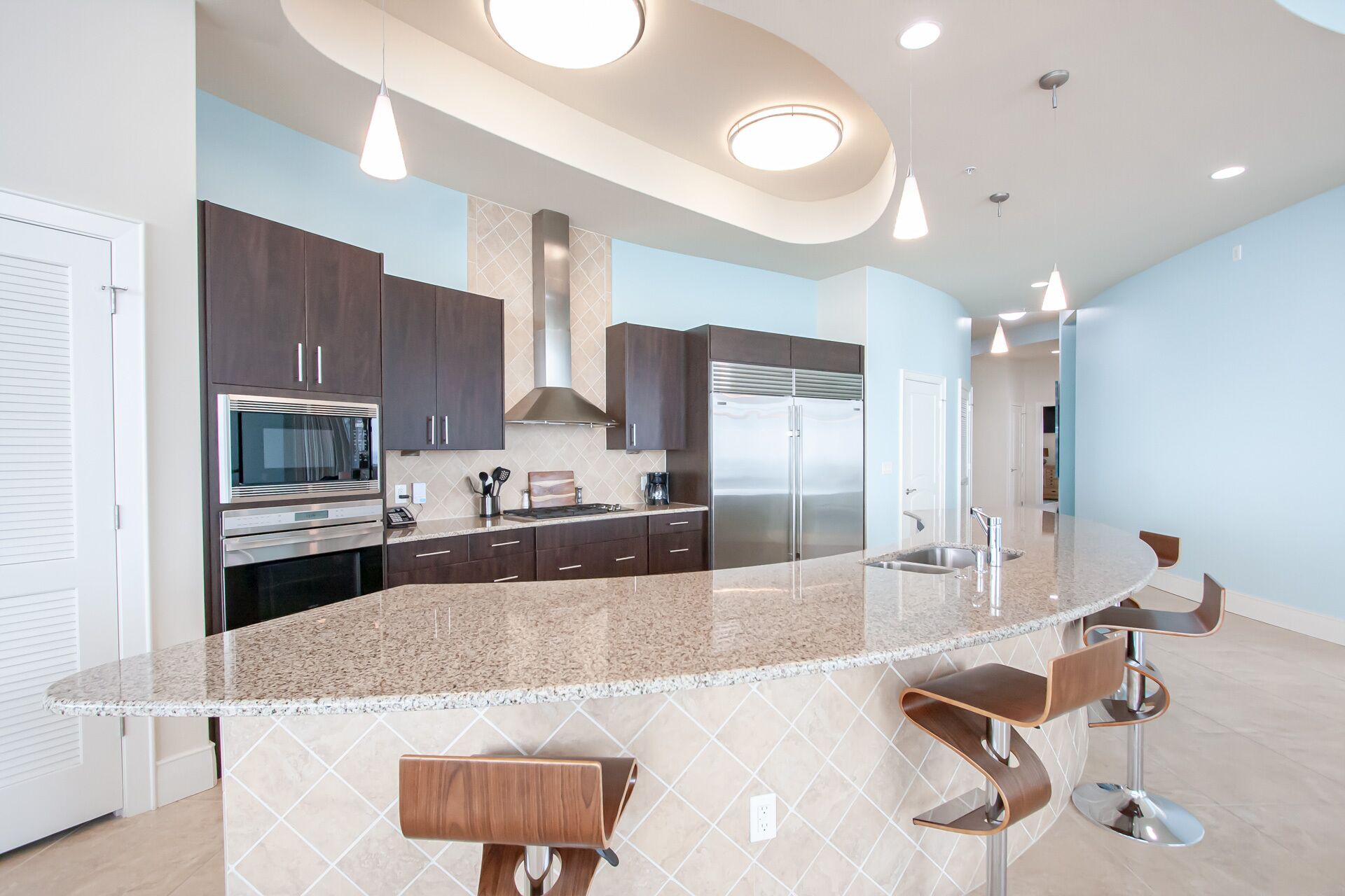A modern kitchen with dark cabinets, stainless steel appliances, a granite countertop, and bar stools.
