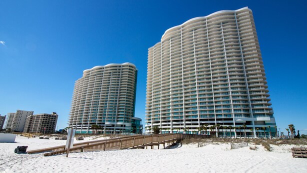 Zwei Hochhäuser mit geschwungener Fassade, in der Nähe eines Sandstrandes mit einem Holzsteg.