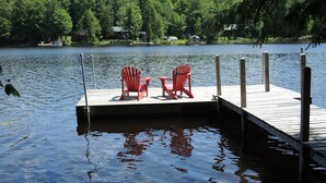 Eine Holzstele führt in einen stillen See, auf der sich zwei rote Adirondack-Stühle befinden.