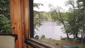 Blick durch ein Fenster mit Holzrahmen auf einen von Bäumen umgebenen See.