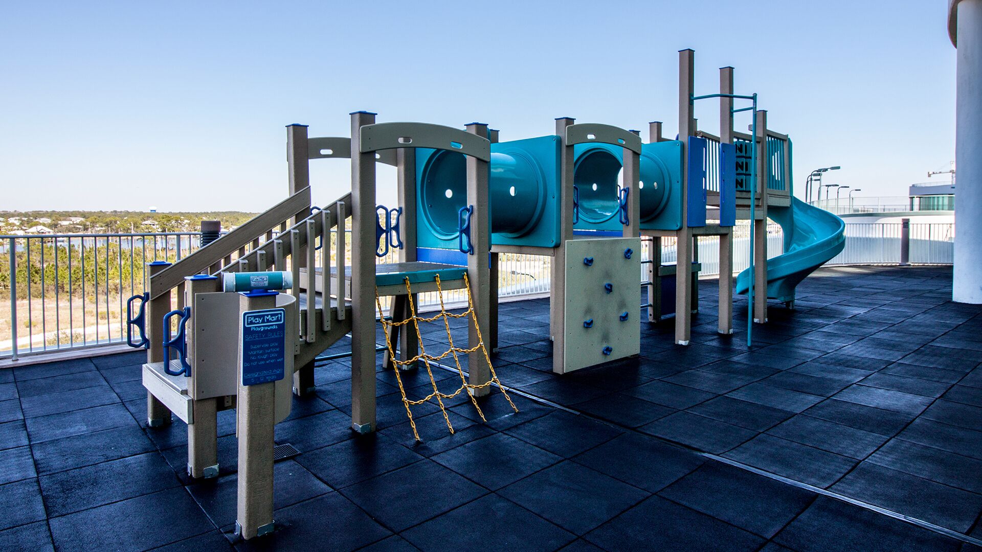 Un parque infantil con tobogán, estructuras para escalar y un letrero de seguridad.