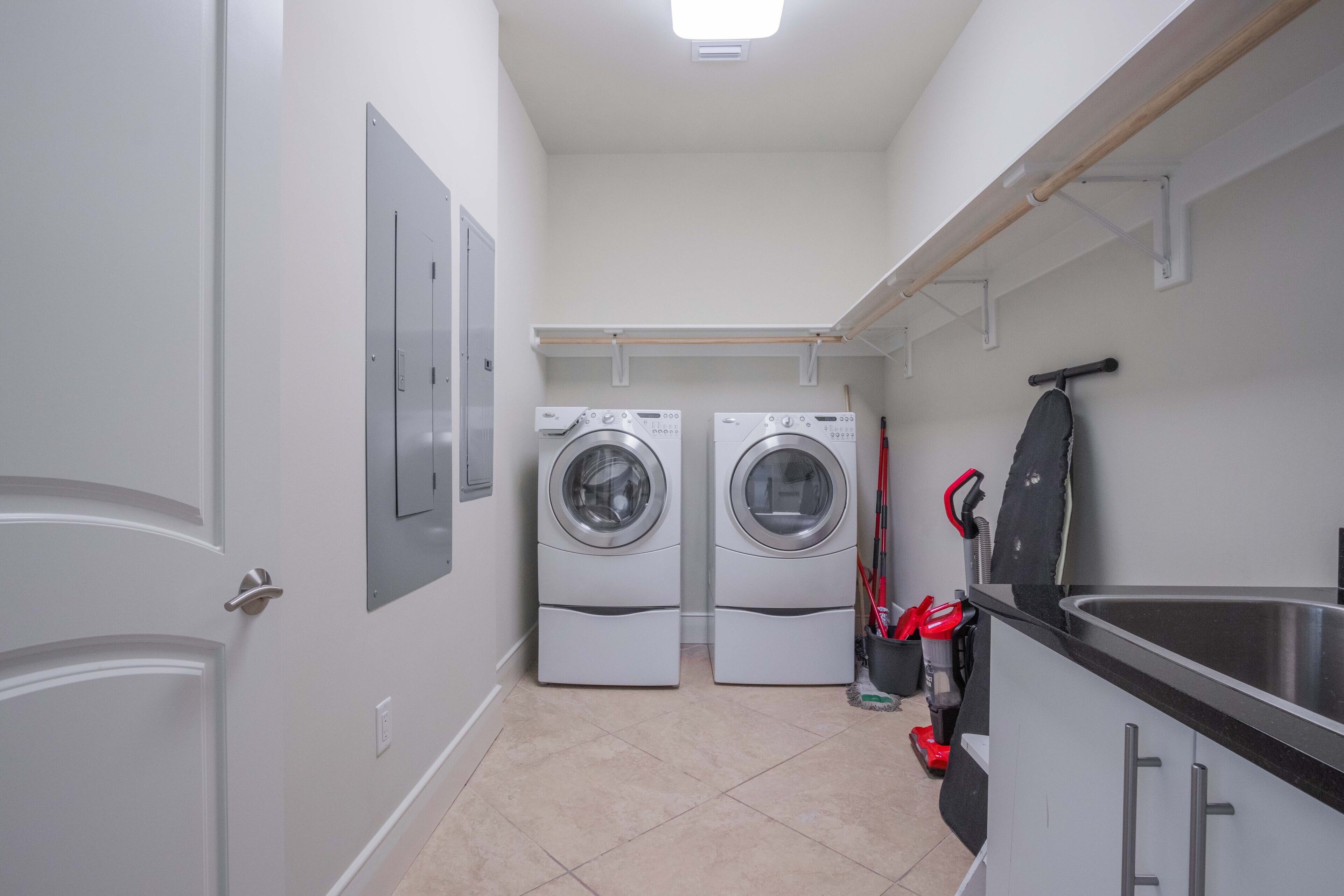 A laundry room with two front-loading washing machines, a sink, and a drying rack.